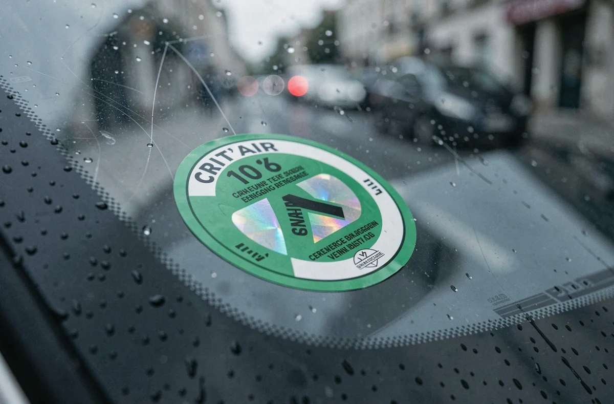 Gros plan sur une vignette Crit'Air verte collée à l'intérieur d'un pare-brise avec la rue française visible en arrière-plan flou