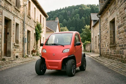 Voiture sans permis rouge garée dans un village des Ardennes avec maisons en pierre et forêt en arrière-plan